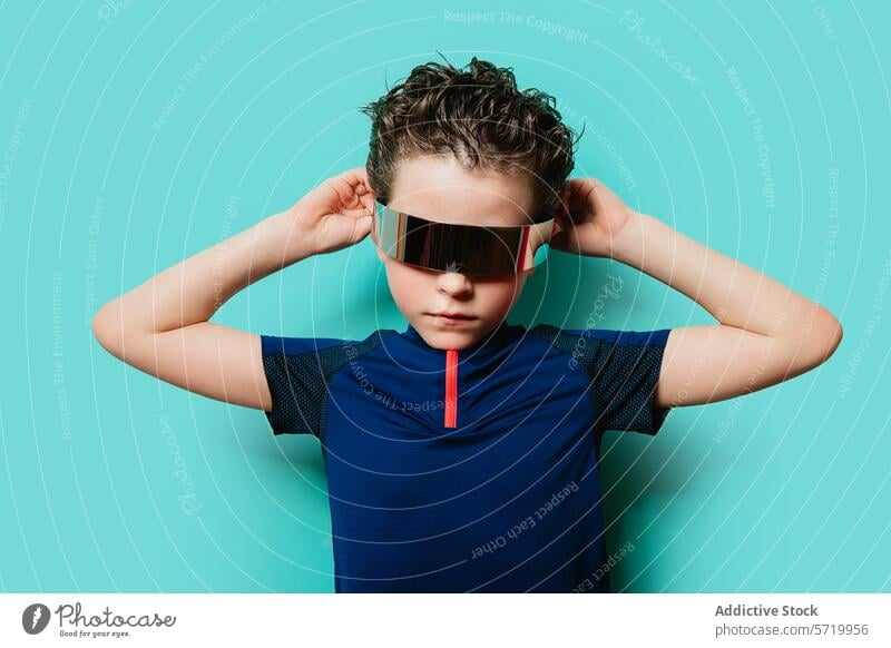 A trendy young boy stands confidently with hands behind head, sporting a futuristic visor against a turquoise backdrop kid cool confidence fashion style youth