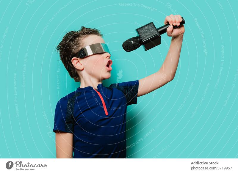 An energetic boy in a futuristic visor and sporty top belts out a tune, poised as if on stage against a teal background singing performance music microphone