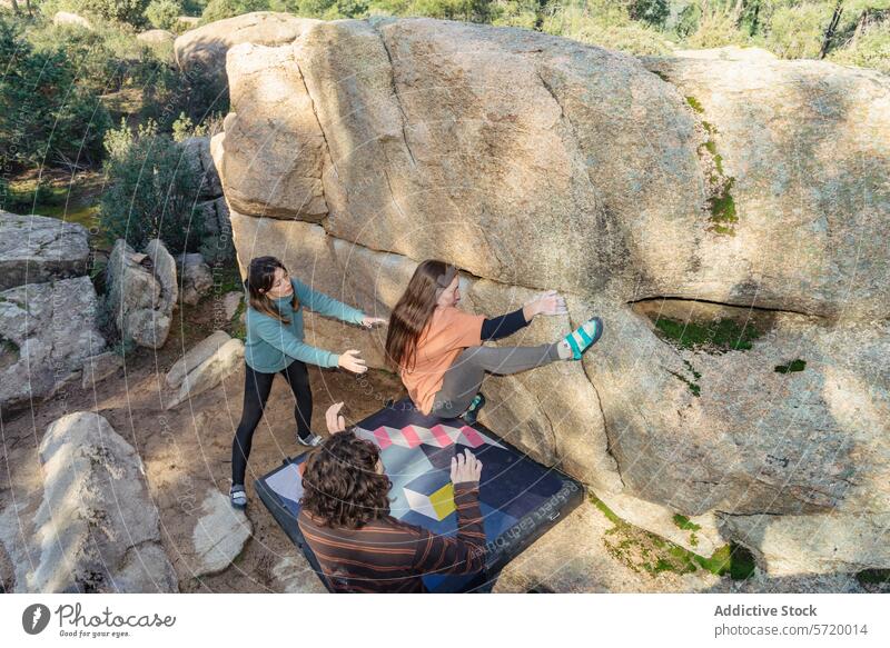 From above of focused climbers work in unison on a boulder problem outdoors, with a spotter ensuring their safety bouldering teamwork rock climbing coordination