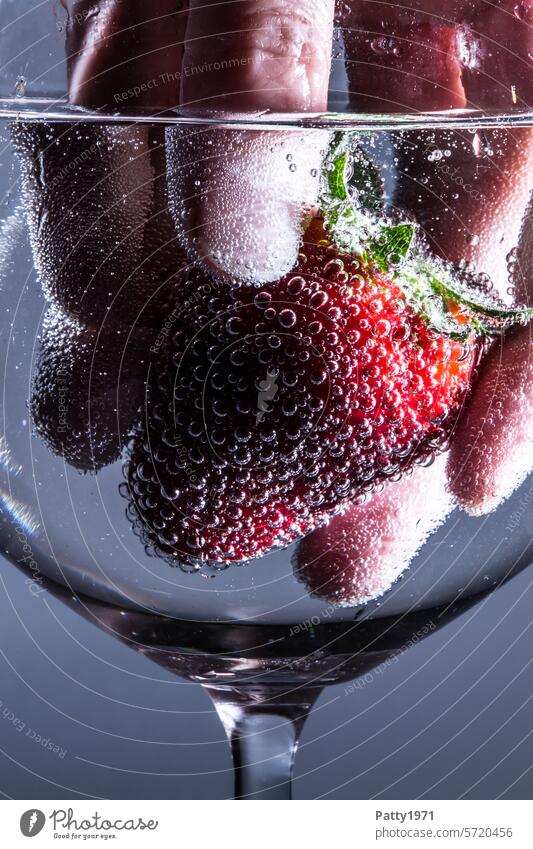 Hand fishes a fresh strawberry out of a jar. Close-up. Food photograph Nutrition Glass fruit blow Fruit Fresh fluid Red food concept Carbonic acid Delicious