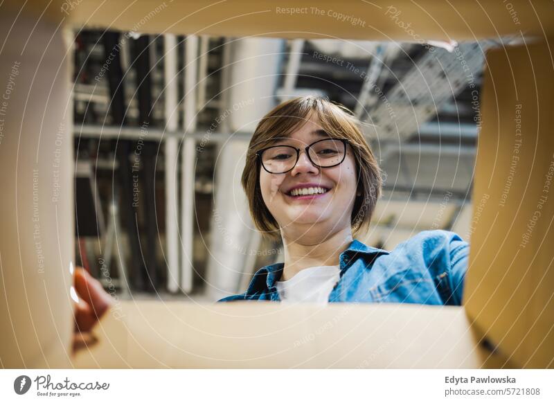 Warehouse female worker looking through an empty box smiling positive emotion standing looking at camera hole office business employee job people profession