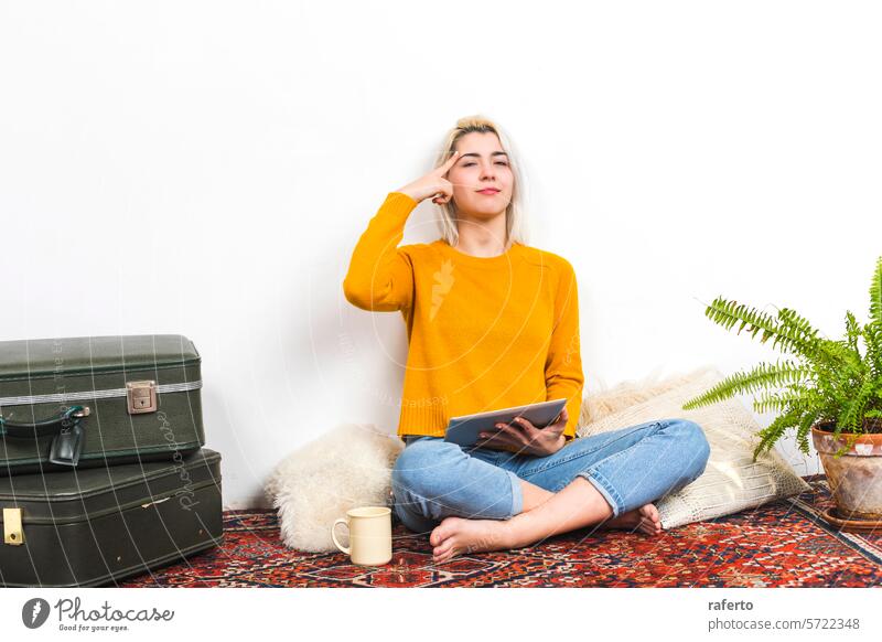 Woman with tablet making a thinking gesture. woman yellow sweater decision contemplation home casual relaxed denim jeans sitting cozy indoor plant