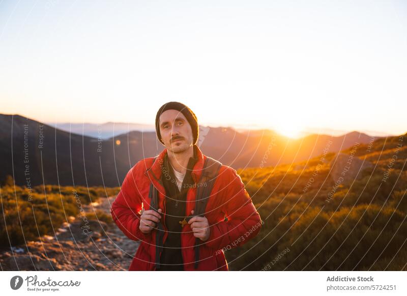 Hiker enjoying the sunset on a mountain trail hiker serene warm glow male red jacket beanie outdoors nature evening light adventure backpack recreational
