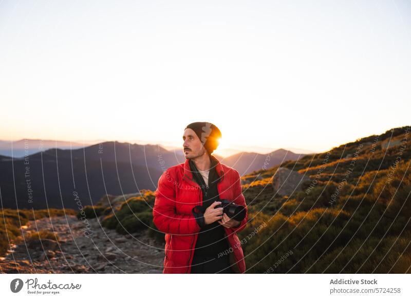 Photographer capturing sunset in mountain landscape photographer camera man red jacket beanie backlight sun rays outdoor adventure nature hobby photography