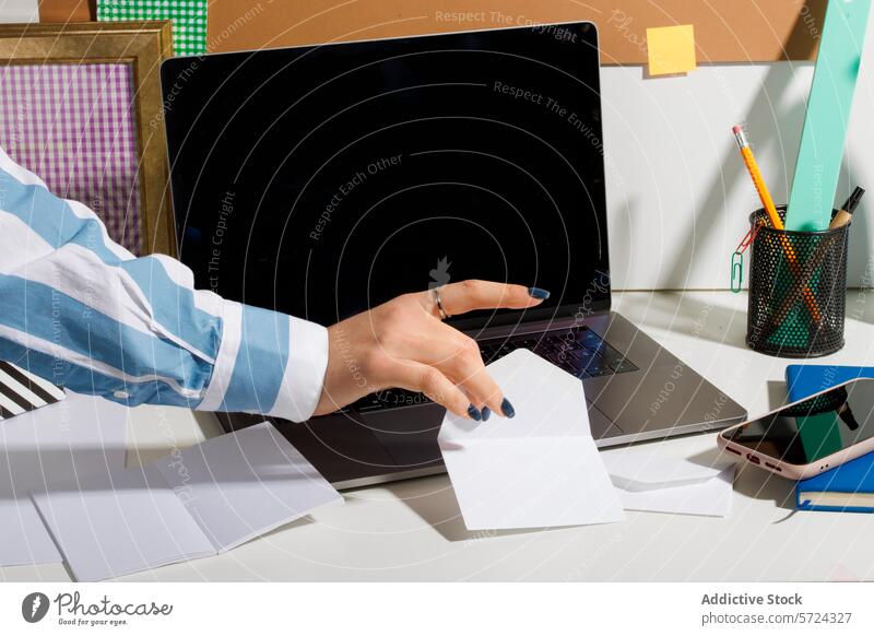 Organized office desk with a person reaching for a paper worker hand laptop organized note grab supply pen holder pencil smartphone post-it paperclip grid frame