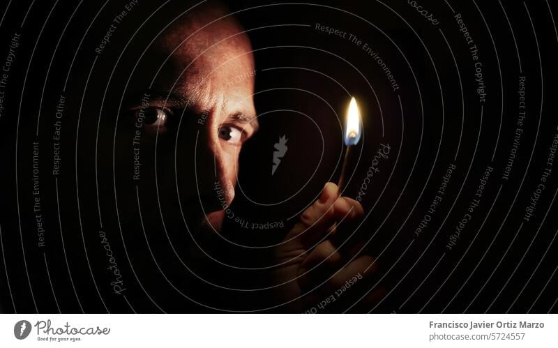 Worried man looking at the camera with a match in the dark. Blackout concept. darkness face blackout electricity flame hand light worried night confused