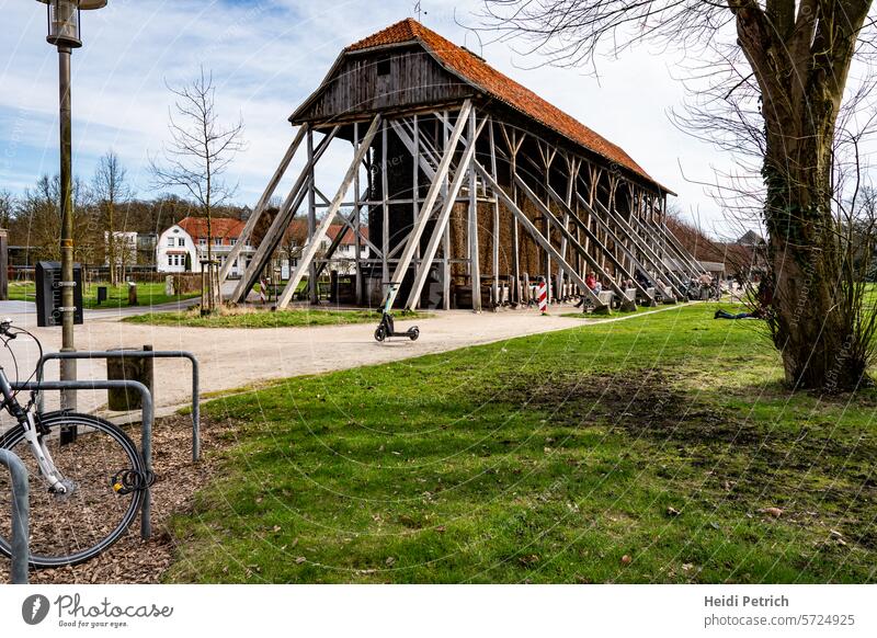 Beautiful weather in Salinenpark, modern meets historical. A bicycle stand, a front wheel, a lantern with a dog bag holder and an electric scooter stand for modern. The wooden building, where salt used to be extracted, is historic.