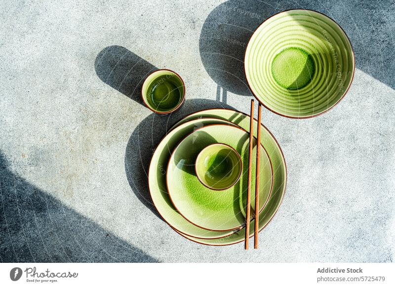 Top view of elegant green ceramic table setting in sunlight top view from above dish bowl cup chopstick shadow texture grey surface bright dinner cutlery meal