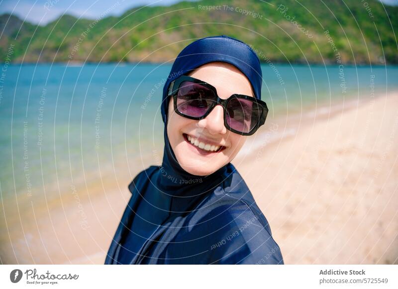Smiling Woman in a Burkini at the Beach woman smiling burkini beach modest swimwear sunbathing sand sunglasses happiness ocean seaside coastal muslim
