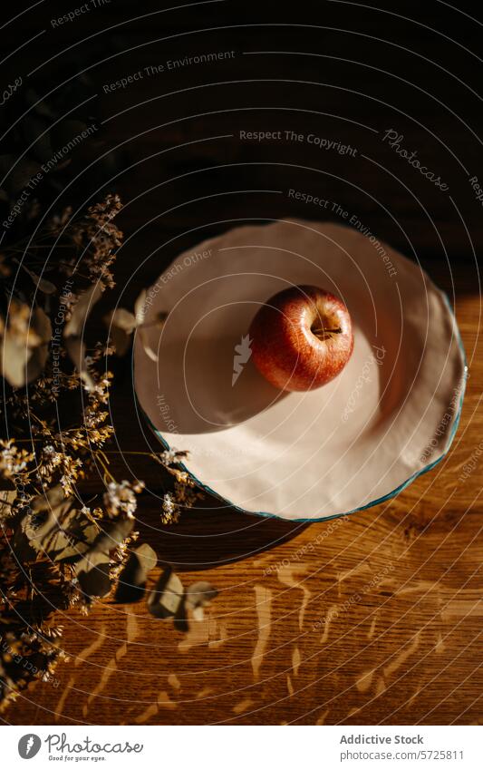 Artistic composition of an apple in dappled sunlight bowl wooden surface shadow dried flower warm still life texture food fruit table shadow play rustic