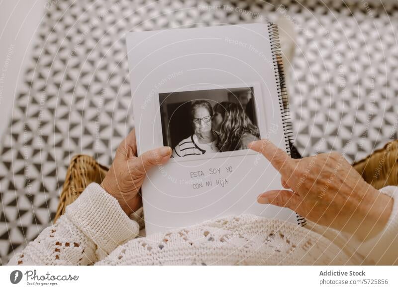 Senior woman holding a photo album with a family picture senior black and white photograph sweater older examine reminiscence memory moment nostalgic personal