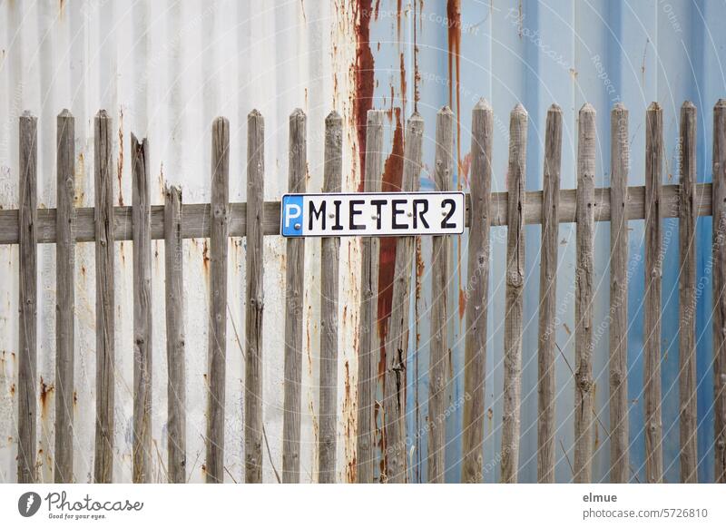 Wooden picket fence with sign P MIETER 2 in front of a rusting sheet metal building Parking lot reserved parking limited parking Tenant parking