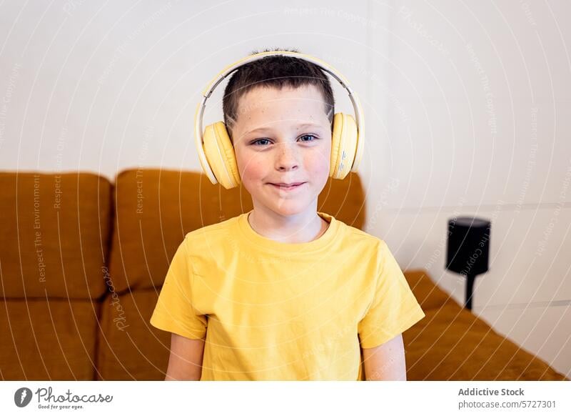 Young boy smiling in yellow headphones at home child t-shirt listening music audio entertainment leisure technology youngster kid happy casual comfort cozy