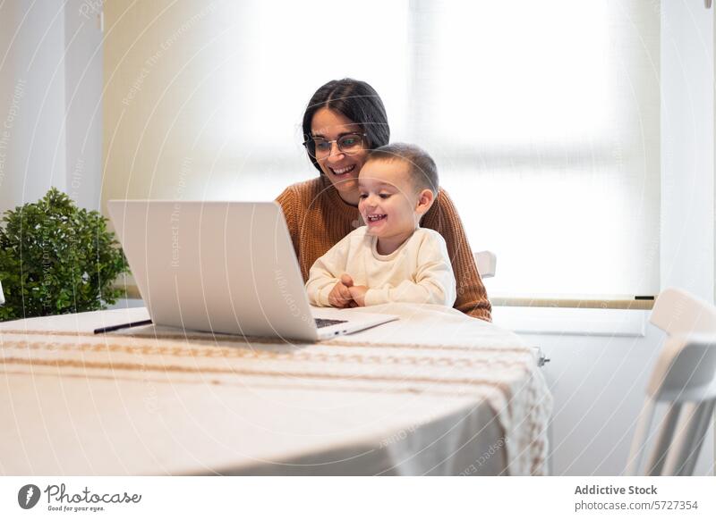 A heartwarming moment as a smiling mother embraces her son while they both engage with content on a laptop at home family togetherness happy happiness work play