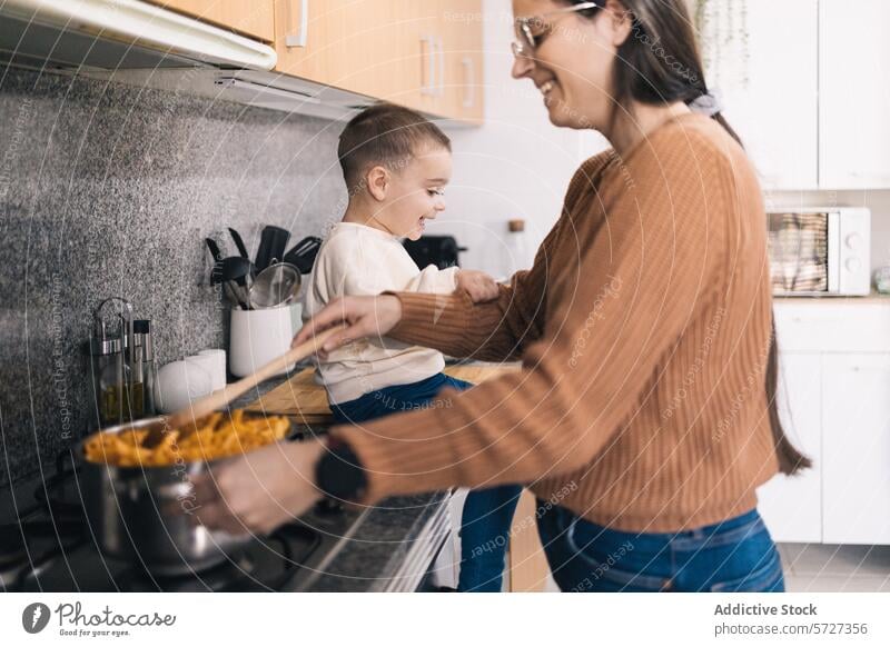 A mother stirs a pot on the stove while her young son watches eagerly, creating a joyful kitchen atmosphere cooking stirring watching interaction bonding family