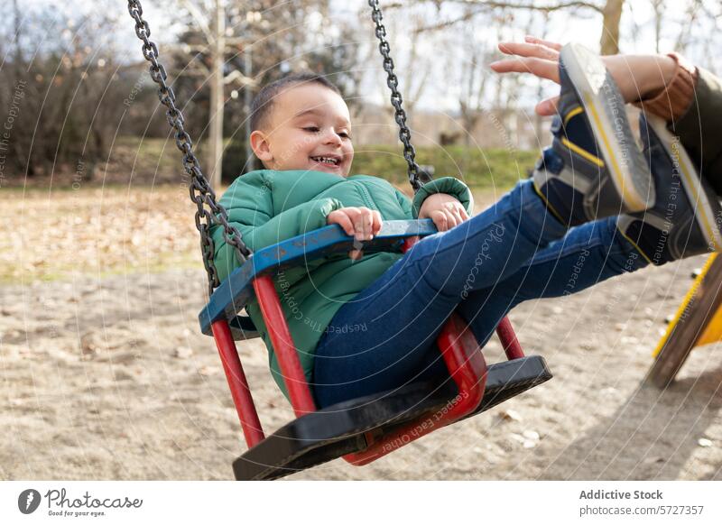 The joyous laughter of a toddler fills the air as he enjoys a swing ride, his feet playfully reaching out to someone just out of view park outdoor fun child