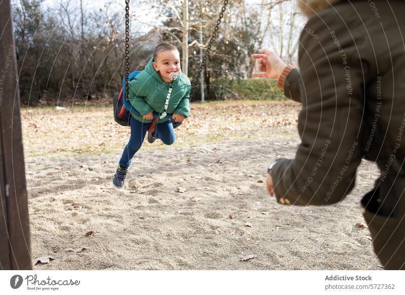 A playful moment captured as a young child giggles while swinging towards an outstretched anonymous hand in a sunny park joy fun outdoor coat laughter movement