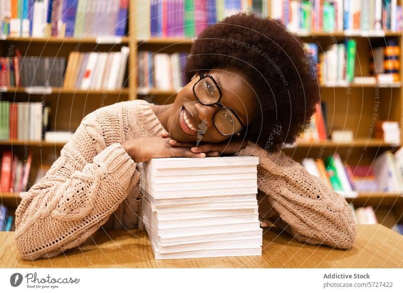 Content African American woman in library with stack of books cheerful head rest literature colorful shelves education reading student study knowledge glasses