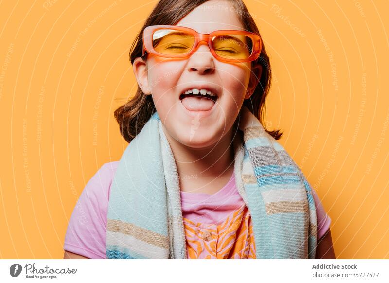 Happy child with colorful glasses sticking out tongue girl cheerful happy orange fun bright background joy playful youth kids expression cute eyewear towel