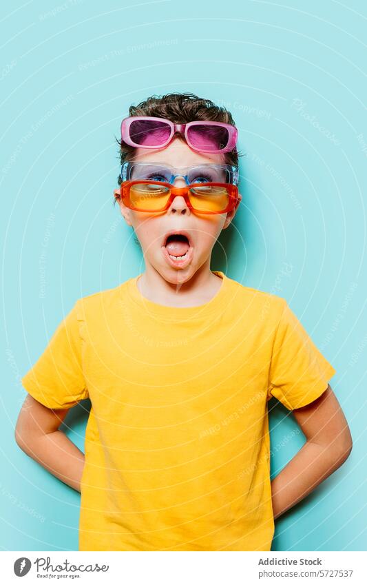 Young boy amazed wearing multiple sunglasses playful expression surprised vibrant turquoise background young child colorful fashion quirky fun eyewear cheerful