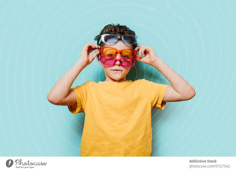 Child with multiple pairs of sunglasses on blue background child boy yellow shirt colorful fashion style quirky accessory kid playful fun eyewear standing