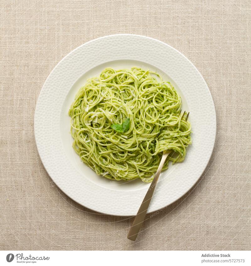 Plate of spaghetti with pesto sauce on a linen tablecloth plate pasta italian food dish meal basil green white beige cuisine dinner lunch vegetarian overhead