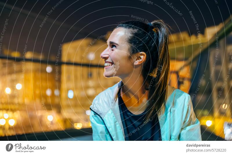 Portrait of cheerful young brunette woman with ponytail looking away in an urban setting at night portrait happy smile female genuine expressing happiness