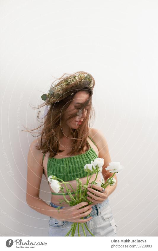 beautiful woman in green crochet handmade top with white flowers and flower headband on white wall minimal background young spring portrait one girl bouquet