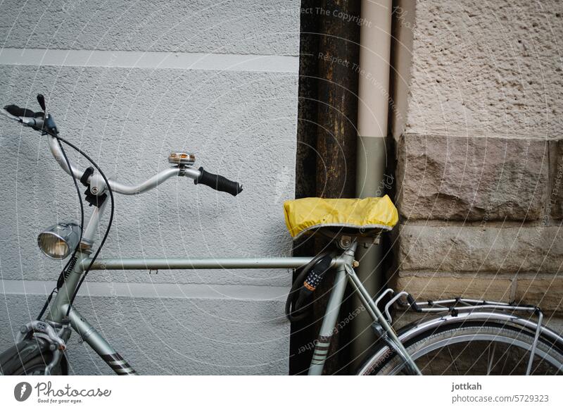 An old men's bicycle with a yellow saddle cover leaning against a house wall Bicycle Transport man's bicycle Wheel Handlebars Saddle Yellow turnaround Cycling