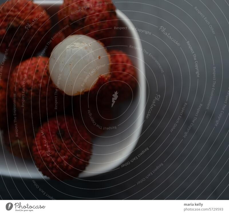 The image is a plate of food containing lychee fruit. It is an indoor shot with red fruits on the plate. spiky lychees bowl white black