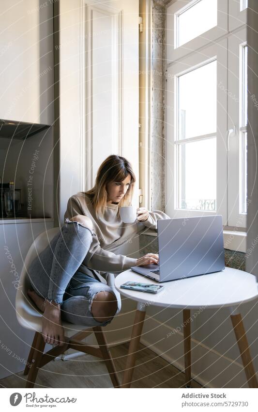 Young woman working from home on a laptop window coffee cup seated room light technology remote work freelance indoors work from home internet business casual