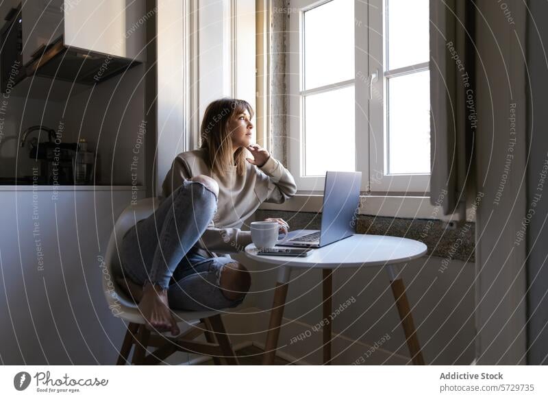 Woman contemplating while working from home near window woman laptop thinking coffee remote contemplation sunlit table chair indoor casual comfort technology
