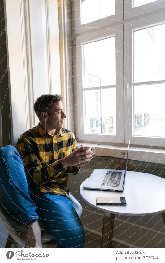 Man relaxing with coffee and laptop by the window man table sitting plaid shirt beverage mug indoor casual technology working browsing peaceful calm serene