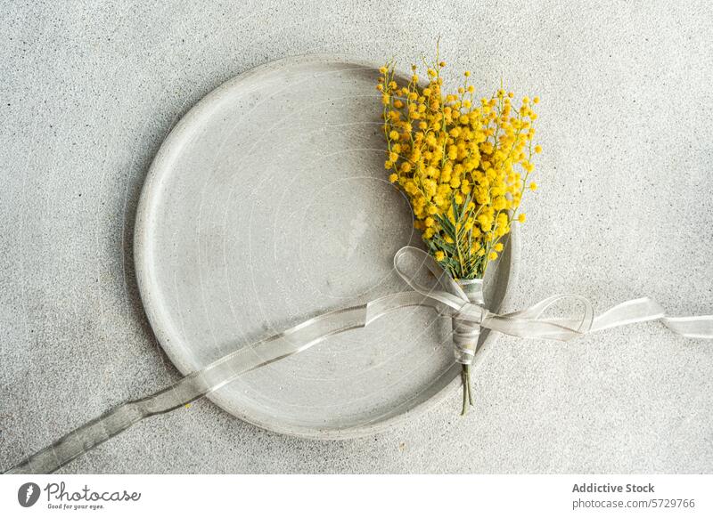 Top view of delicate arrangement of vibrant mimosa flowers tied with a silver ribbon, presented on a sleek, textured table surface for a sophisticated touch