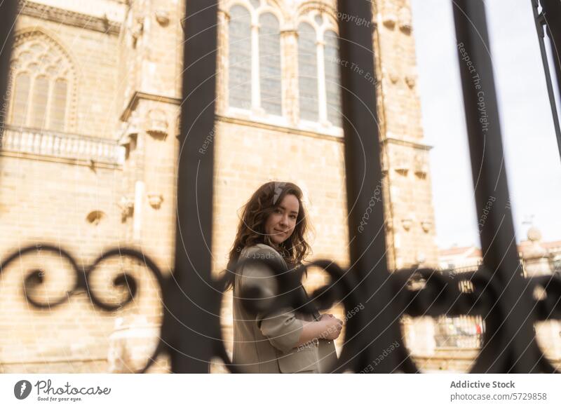 A woman offers a gentle look through ornate wrought iron gates with the historic facade of a cathedral as her backdrop gaze elegant architecture heritage style