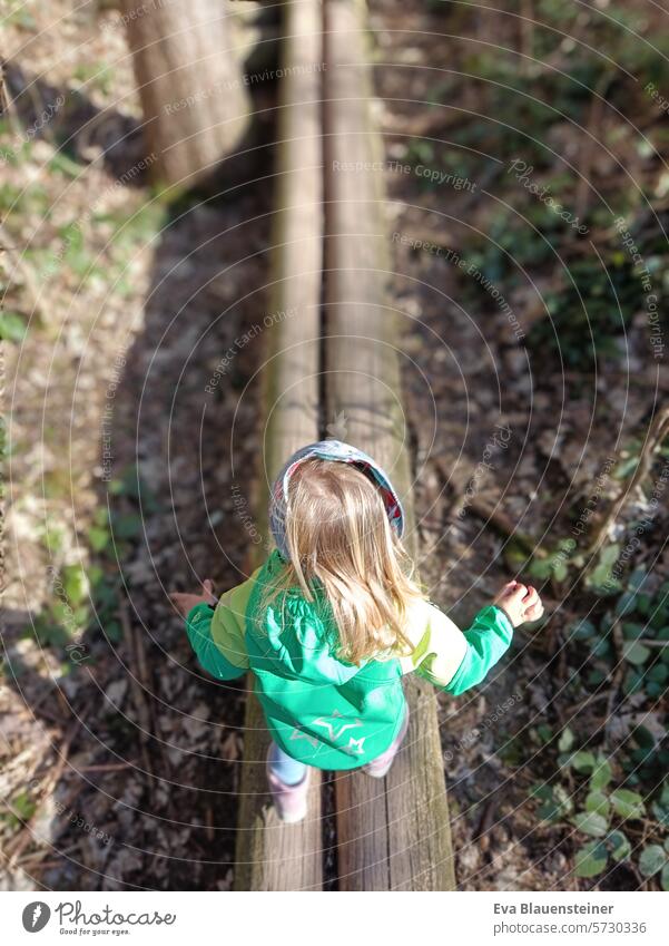 Toddler in green jacket balancing on two wooden beams in the forest balance Forest Child Above Wood Woodground