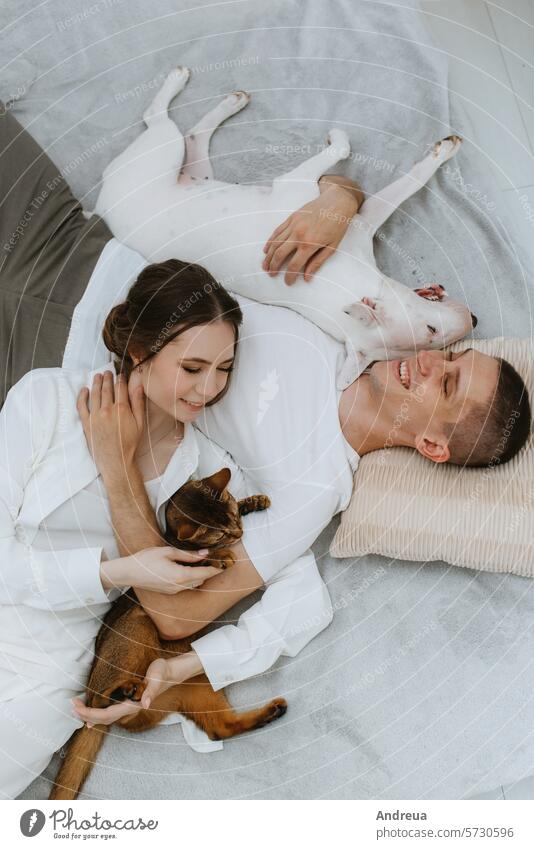 young couple guy and girl in a bright room playing with pets white dog smooth wool light brick wall corner grey tile tail friend man's friend pink teeth tongue