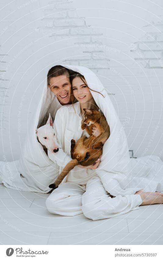 young couple guy and girl in a bright room playing with pets white dog smooth wool light brick wall corner grey tile tail friend man's friend pink teeth tongue