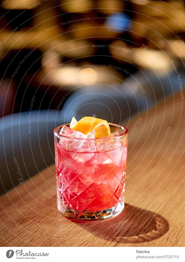 Transparent pink alcohol cocktail, vodka gin-tonic orange zest spiral gin-tonik transparent glass bar counter decorated drink copy space ice beverage red orange