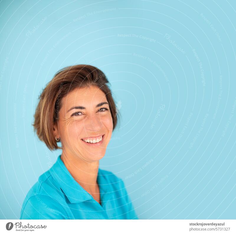 A woman, owner of her own physiotherapy clinic, smiles confidently, on a plain blue background physiotherapist female women portrait contented self confident