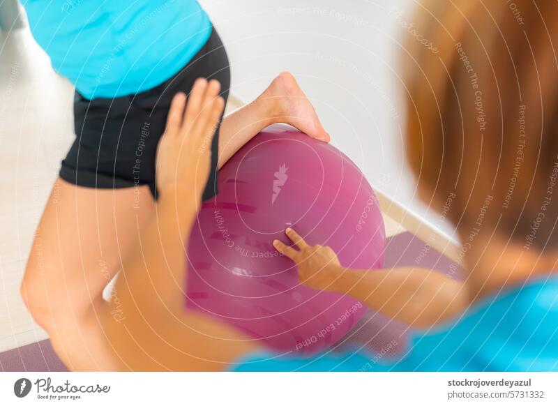 A physiotherapist helps a patient, during an exercise with a fitness ball, in a therapeutic Pilates workout session fitball clinic rehabilitation health care