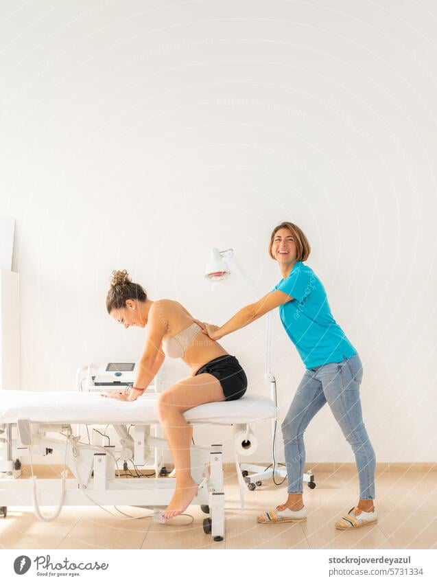 A physical therapist smiles happily as she presses on her patient's back during a manual therapy session physiotherapist clinic rehabilitation health care