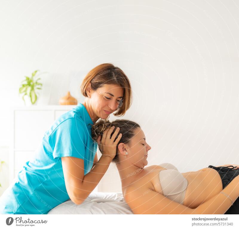 A female physiotherapist performs a stretching exercise on her patient's neck, lying and relaxed on the table clinic rehabilitation health care physiotherapy