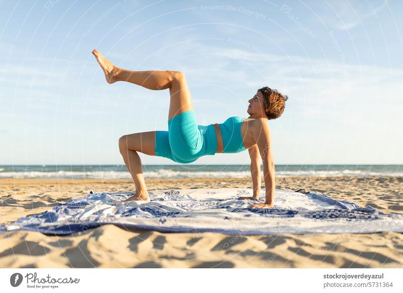 A woman practices Pilates exercises on the beach and performs a leg pull back movement pilates yoga mediterranean spain mind-body exercise contrology sunset