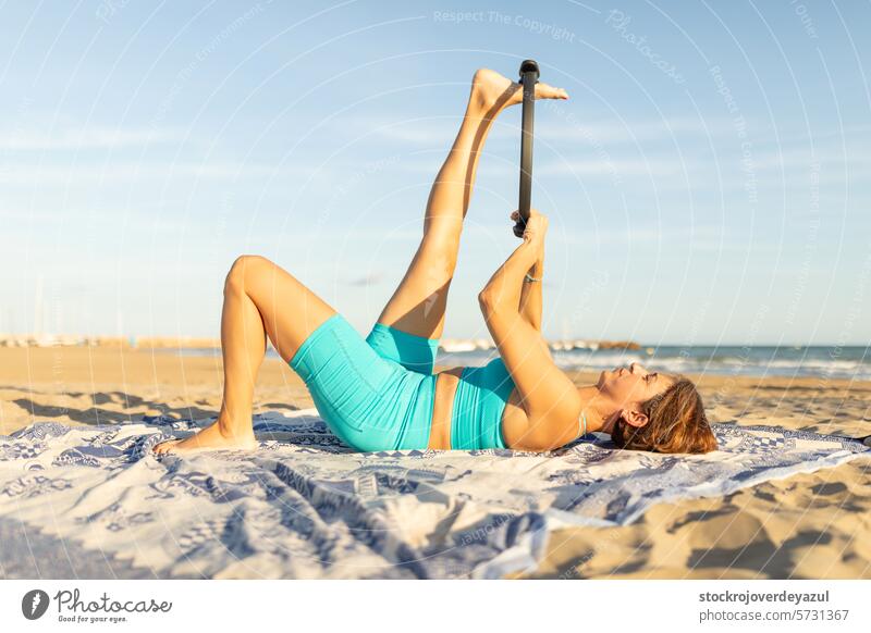 A woman performs Pilates exercises with a Pilates ring on the beach, to stretching legs pilates ring yoga mediterranean spain mind-body exercise contrology