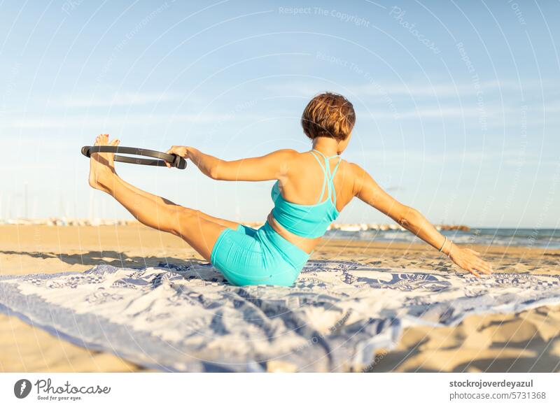 A woman performs Pilates exercises with a Pilates ring on the beach, to stay fit pilates ring yoga mediterranean spain mind-body exercise sunset sea sport
