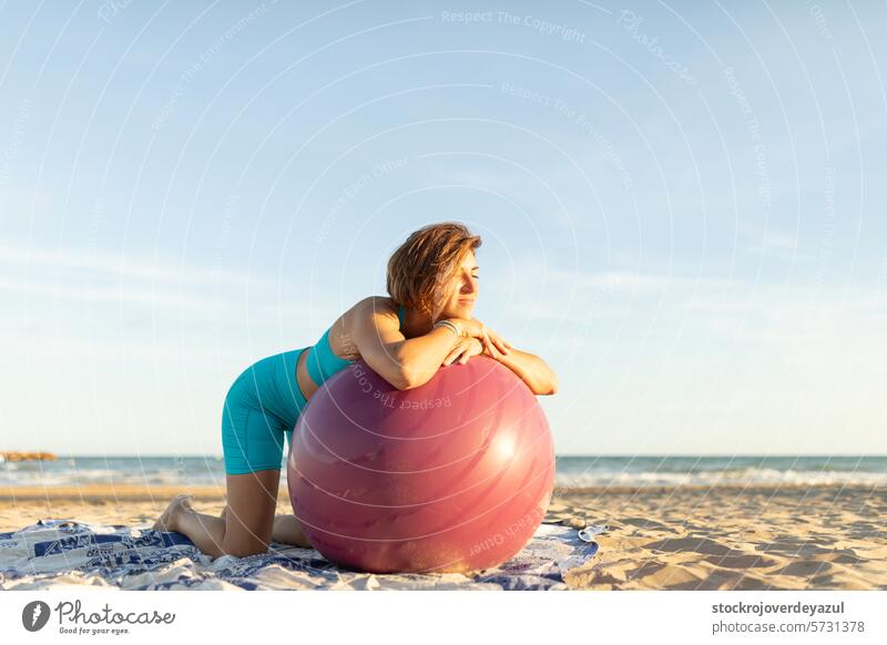 A woman rests and relaxes during a Pilates session on the beach, leaning on a Pilates ball exercise pilates mediterranean spain mind-body exercise sunset