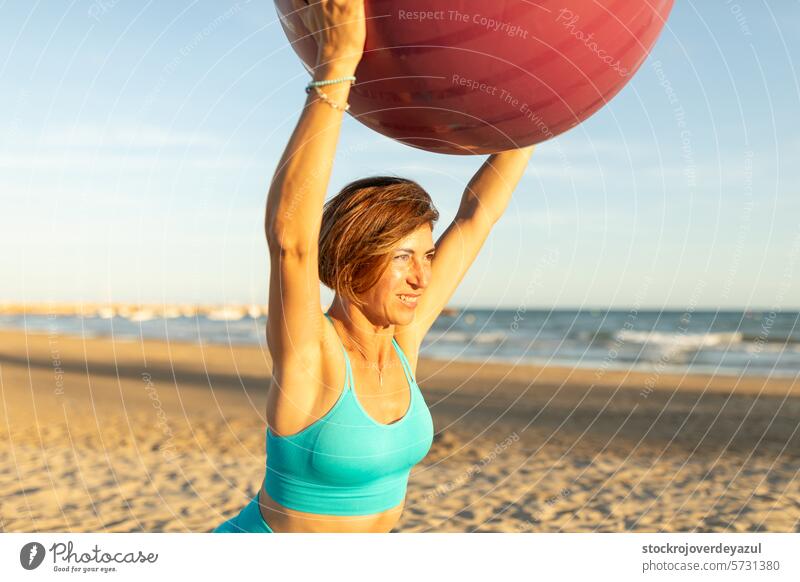A woman performs stretching and balance exercises with a Pilates ball during a session on the beach pilates mediterranean spain mind-body exercise contrology