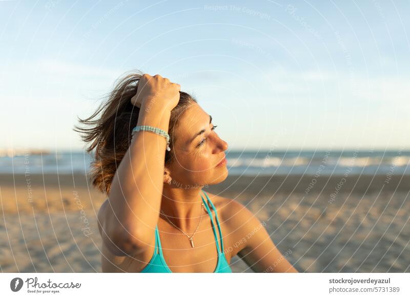 A woman strokes her hair while enjoying the last rays of the sun, after a Pilates session on the beach exercise pilates mediterranean spain mind-body exercise