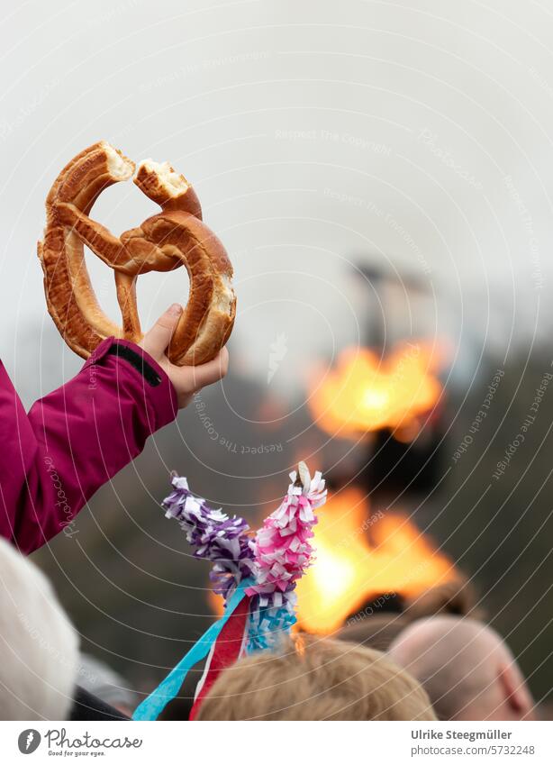 A child holds a bitten pretzel behind which a snowman is burning, symbolizing the beginning of spring Summer day parade Speyer palatinate Rhineland-Palatinate